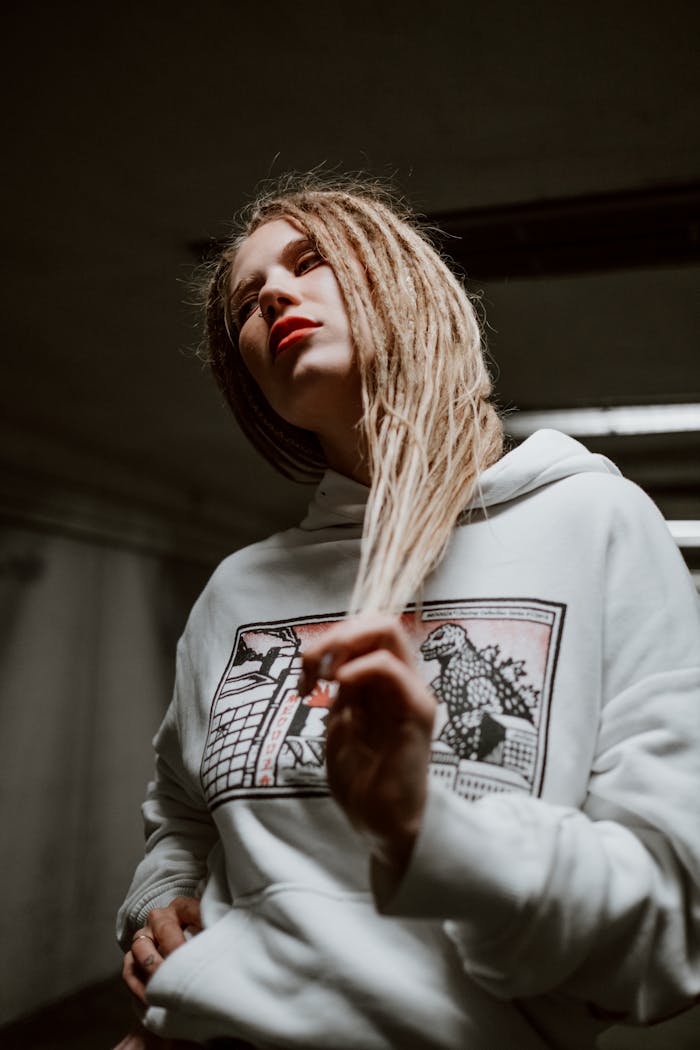 Portrait of a woman with dreadlocks wearing a graphic white hoodie indoors, exuding urban style.